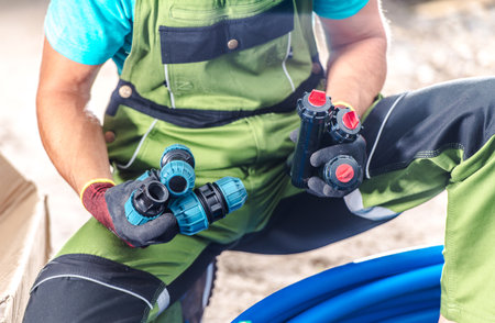 A worker focuses on assembling blue plumbing pipes and fittings in a busy construction site during daylight hours, showing precision and attention to detail.の写真素材
