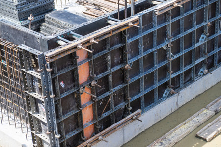 Workers are installing concrete formwork and reinforcement at a construction site near a body of...