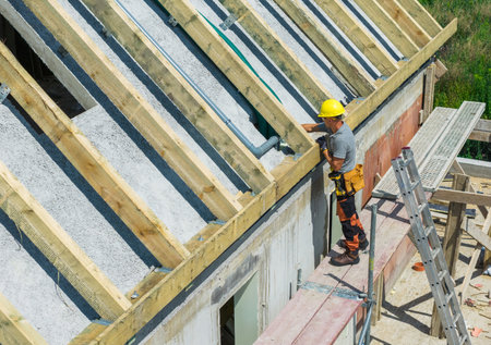 Construction worker carefully positions roof beams on a new residential building during a sunny day,...