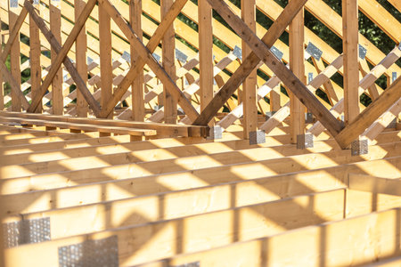 Workers are constructing a wooden framework for a house, showcasing beams and supports under the...
