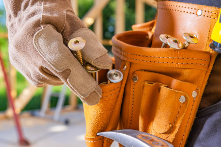 A skilled worker organizes screws in a tool belt while working at a construction site.