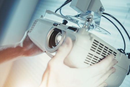 A technician carefully installs a projector in a bright office setting, ensuring the device is...