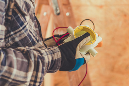 A technician holds a multimeter while wearing gloves, examining electrical readings on a construction site in bright daylight.の写真素材