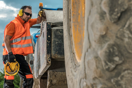 A construction worker in safety gear examines heavy machinery during daylight, focused on ensuring...