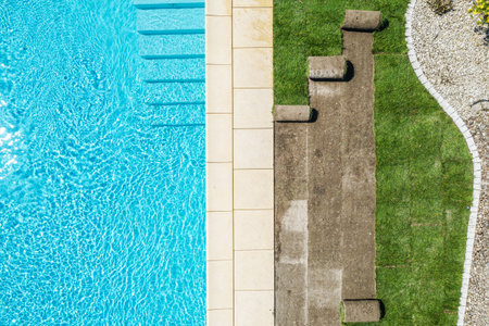 A bright and inviting swimming pool area features clear blue water, stone tiles, and grassy patches...