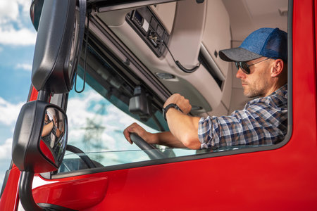 A truck driver in a red vehicle monitors his watch, exhibiting a watchful demeanor while parked at a...