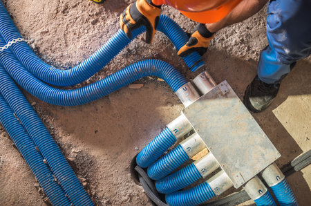 A worker assembles blue piping on the ground at a construction site, focusing intently while...