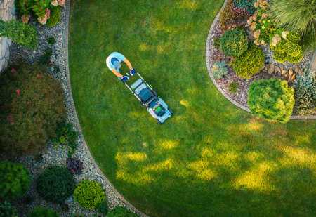 A person speaks a lush green lawn in a beautifully landscaped garden with flowerbeds and decorative plants during bright daylight.の写真素材