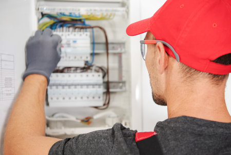 A skilled electrician inspects and repairs a residential circuit box, ensuring proper electrical connections and safety measures in a home environment.の写真素材