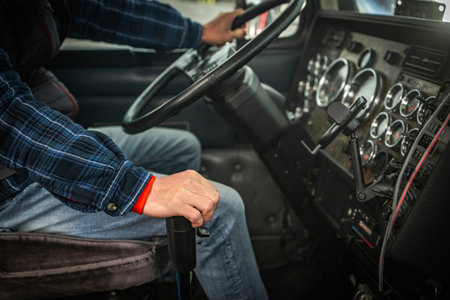A driver grips the steering wheel while shifting gears inside a large truck's cabin. The environment is focused and bustling with activity.の写真素材