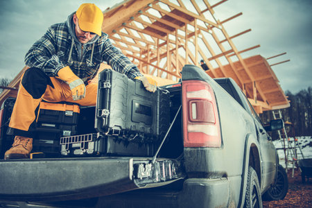 A construction worker in warm clothing arranges tools in the truck bed while working on a building site. Snow can be seen in the background.の写真素材
