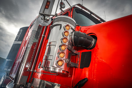 A vibrant red truck showcases its polished chrome accents under a dramatic sky during the afternoon.