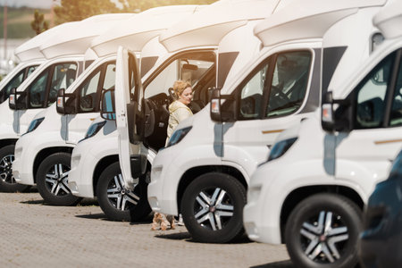 A young woman stands beside a camper van with its door open, examining the vehicle at an outdoor market on a sunny day.の写真素材