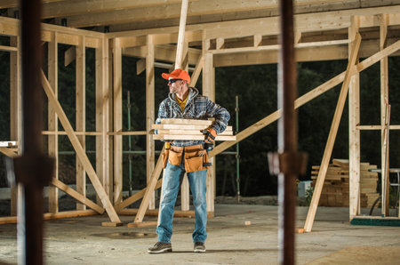 A worker holds wooden planks at a construction site with wooden frames in place. Tools are visible...