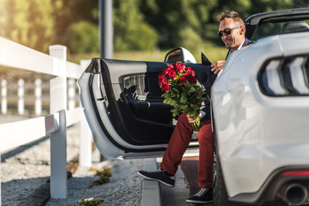 A man sits in a white car with a bouquet of roses, preparing to step out on a sunny day at a roadside.の写真素材