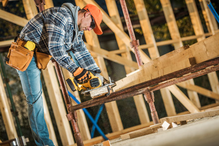 A worker uses a saw to cut wood on a construction site with scaffolding and tools.