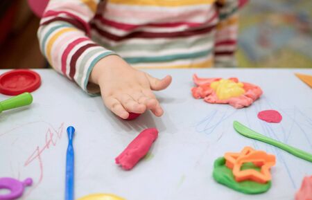 Child hands playing with colorful clay. Plasticine. play dough, social distance quarantine Covid-19, self-isolation, online education concept, homeschooling. Toddler girl at home, kindergarden closed.の写真素材