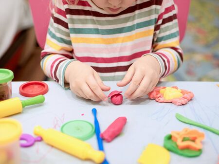 Child hands playing with colorful clay. Plasticine. play dough, social distance quarantine Covid-19, self-isolation, online education concept, homeschooling. Toddler girl at home, kindergarden closed.の写真素材