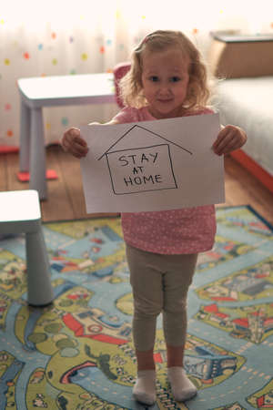 Child showing paper words stay at home during a coronavirus epidemic. Covid-19 outbreak concept. Hashtag stayhome. Stay work at home, social distance, selfisolated.の写真素材