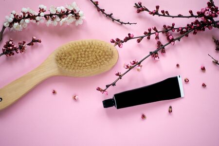 Massage brush and skincare cream isolated on pink coloured background with sprig first flower...