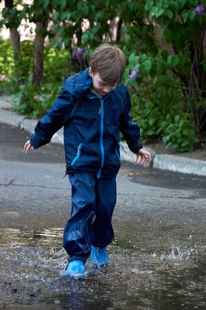 Happy child jumping in puddle in waterproof coat. A boy have fun in the rain weather in a bright raincoat. Legs of child with rubber boots.の写真素材