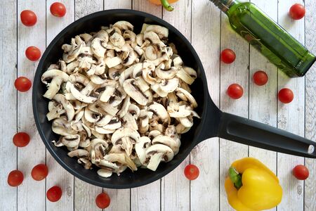 Pan with mushrooms on a kitchen table on wooden culinary background. Top view, yellow papers and cherry tomatos and olive oil around.の写真素材