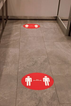 Red round sign printed on ground at supermarket cash desk register informing people to keep 2 meter...