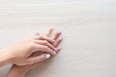 Stylish trendy female pastel white, pink and blue manicure. Beautiful young woman's hands on wooden background. Copy space banner.の写真素材