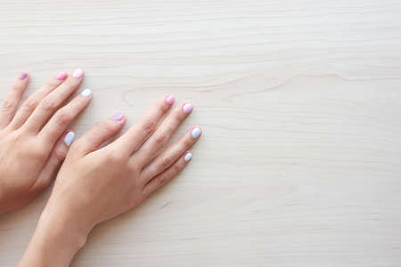 Stylish trendy female pastel white, pink and blue manicure. Beautiful young woman's hands on wooden background. Copy space banner.の写真素材