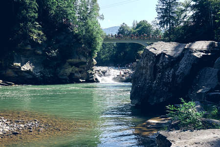 A waterfall flowing down from a Sheer cliffs . Blue clear water of mountain the river. Rocky stones and forest Alpine landscapeの写真素材