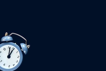 Blue vintage alarm clock shows 12 oclock isolated on dark background. Wake up and hurry up. Hot...