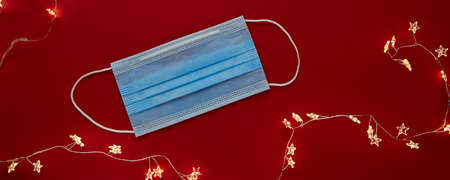 Festive coronavirus face mask with decorations and ligths on red background. Flat lay, top view...