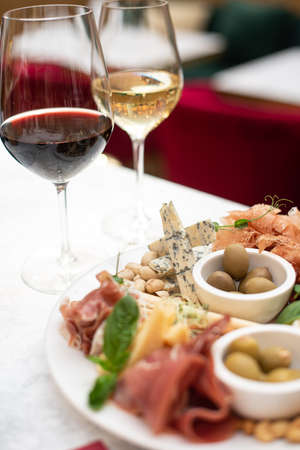 Assorted snacks. Cheese appetizer, cured meats, olives with two glasses of red and white wine in restaurant or cafeの写真素材