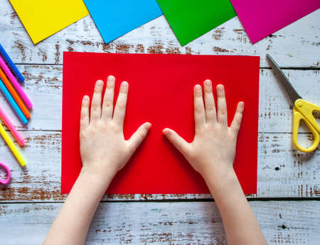 The childs hands are on a sheet of red colored chalk paperon the tableの写真素材