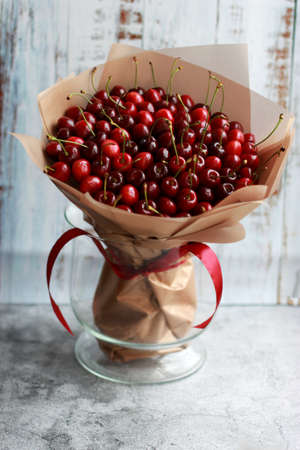 Bright edible round bouquet of cherry berries on the base, wrapped in gold film and tied with a ribbon as an unusual gift. Foodfloristics. Selective focus.の写真素材