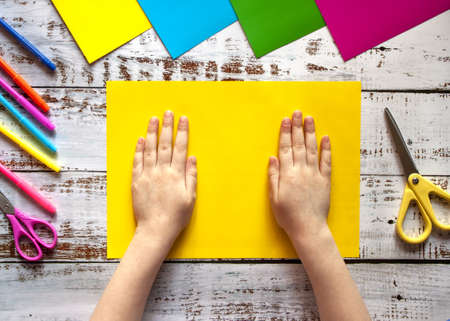 Childrens hands, ready for creativity, lying on a sheet of yellow colored paperの写真素材