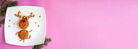 Funny Christmas new years deer of food: cookies, bread, pretzels, candy on a white square plate with snowflakes on a pink background and space for text. Banner for new year and Christmas.の写真素材