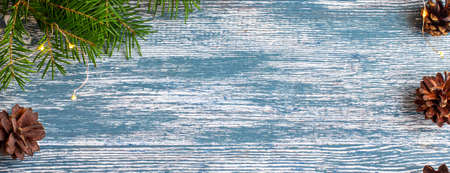 Christmas background of wooden planks painted in blue with fir branches, garland and cones on the...