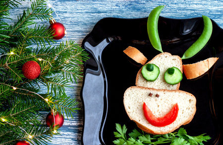 Creative Breakfast sandwich of peas, tomatoes, parsley, cloves, spices, cucumber in the form of a bulls head with large horns on a blue table and fir branches with red balls.の写真素材