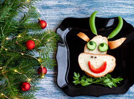 Funny sandwich of loaf, tomato, cucumbers, peas, cloves, parsley in the form of a bulls head or a cow, the symbol of 2021 New year and Christmas on a black plate on a blue background ana red ballの写真素材