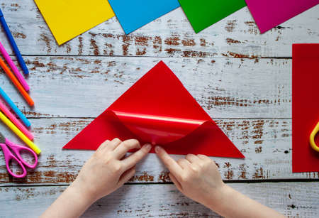The hands of a child making origami from colored red paperの写真素材