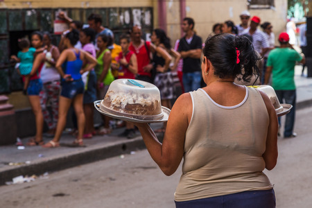 Heads turn in a queue on the street in Havana as a woman carries a couple of large cakes home from a shop.  They looked very tasty & sweet - steeped in icing.の写真素材