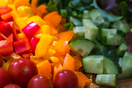 Red, amber & green coloured vegetables make up a colourful English salad - seen on a wooden board.の写真素材