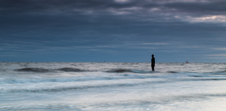 The incoming tide swirls around an Iron Man on Crosby beach.  This is one of 100 cast iron statues modelled on & created by Anthony Gormley which are dotted along the beach.の写真素材