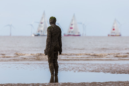 An Iron Man watches the start of the 2017/18 round the world Clipper race on a beach near Liverpool.The Clipper Race (now in its eleventh year) sees twelve global teams compete in a 40000 nautical mile around the world race on a 70 foot ocean racing yachtのeditorial素材