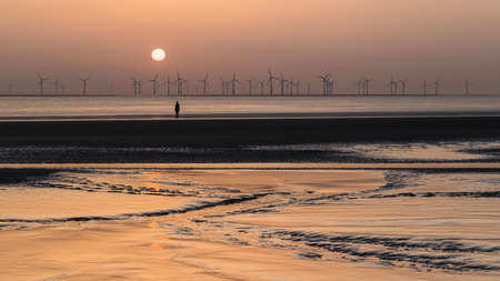 An Iron Man stands on the shore at Crosby Beach.  This is one of the one hundred Iron Men statues which make up Antony Gormley's Another Place art installation captured on Crosby Beach near Liverpool at sunset in April 2021.のeditorial素材