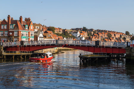 Red fishing boat travels under the swing bridge in Whitby at high tide captured in September 2020.のeditorial素材