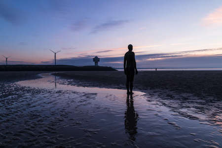 The light begins to fade on the beach at Crosby near Liverpool as a lone figure from the Iron Men installation faces out to sea.のeditorial素材