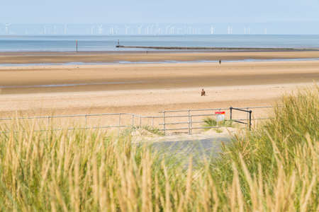 Three of the one hundred Iron Men figured known as Another Place pictured on Crosby beach near Liverpool in August 2021 seen over the sand dunes.  These statues were modeled on and created by Antony Gormley.のeditorial素材