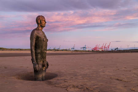 High cloud above an Iron Man lit up in pink and puple light at sunset on Crosby beach near Liverpool in September 2021.  He is one of the 100 Iron Men statues created by Antony Gormley which occupy this stretch of the Sefton coastline.のeditorial素材